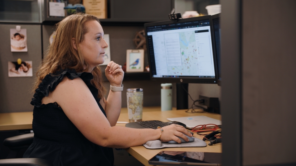 GIS analyst sitting at desk working on computer with a map on the screen.