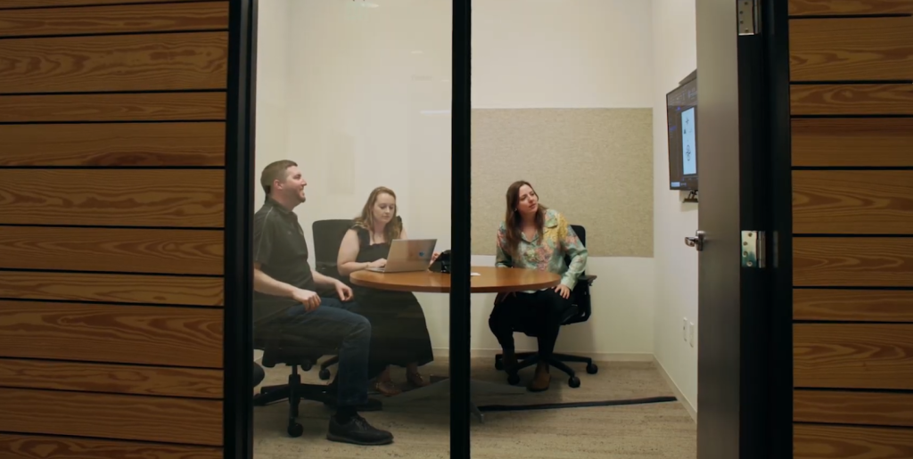Team of employees sitting in an office looking at a screen. 