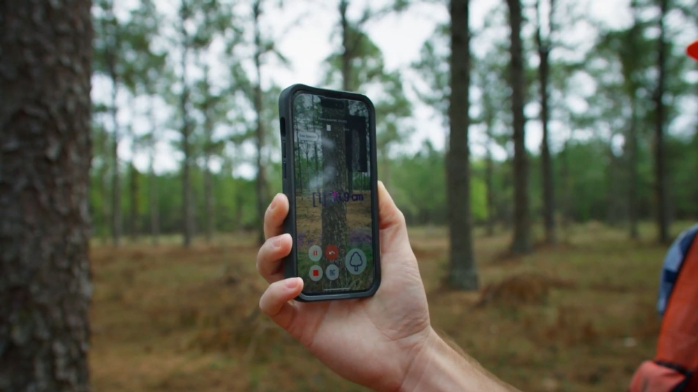 Someone in a forest holds a phone running a LiDAR app